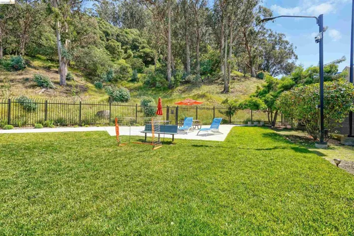 Expansive lawn area with a concrete patio, bordered by a black metal fence