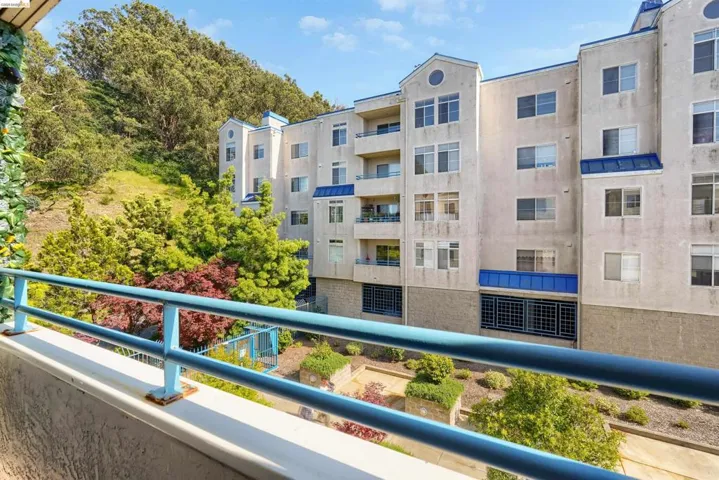 Balcony with blue railings overlooking a multi-story building and landscaped grounds