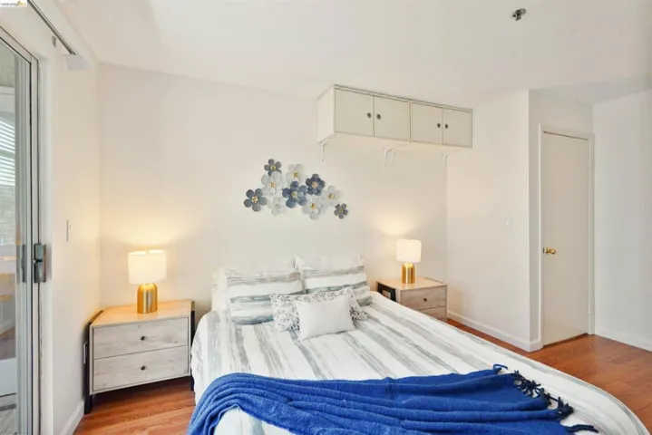 Hardwood flooring extends throughout this room, featuring a built-in wall cabinet with four doors, a white door with a brass-finish knob, and a sliding glass door providing external access