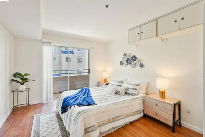 Wood-finish flooring throughout, featuring a full-width balcony with sliding glass doors, built-in overhead cabinetry, and two-drawer nightstands
