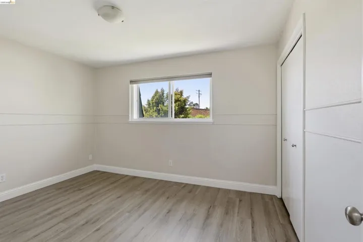 Spacious room featuring wood-finish flooring, a double-panel window, baseboard trim, and a bi-fold closet with contemporary doors