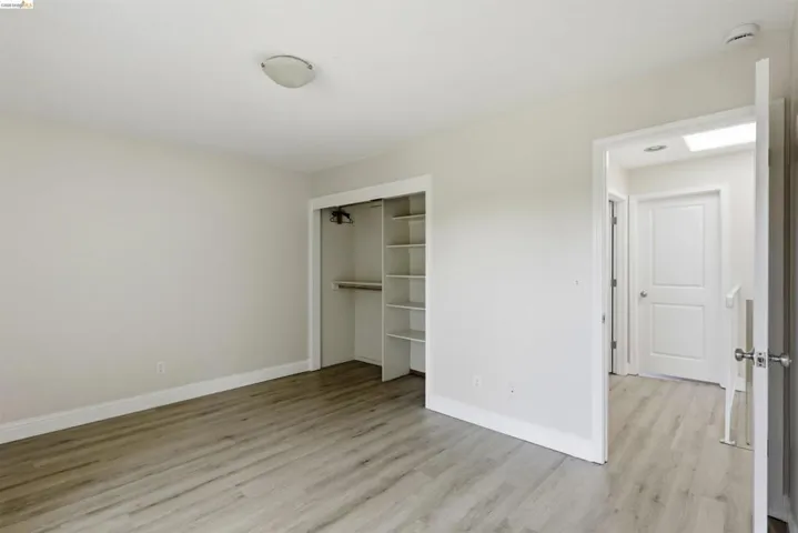 Room featuring wood-finish flooring, a built-in closet with shelving and hanging rod, light neutral wall paint, and white trim
