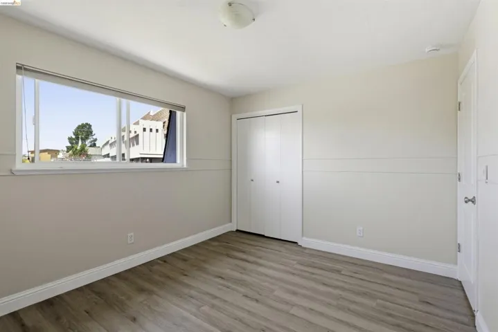 Spacious interior featuring wood-finish flooring, a broad window, white baseboards, and a built-in closet with bifold doors