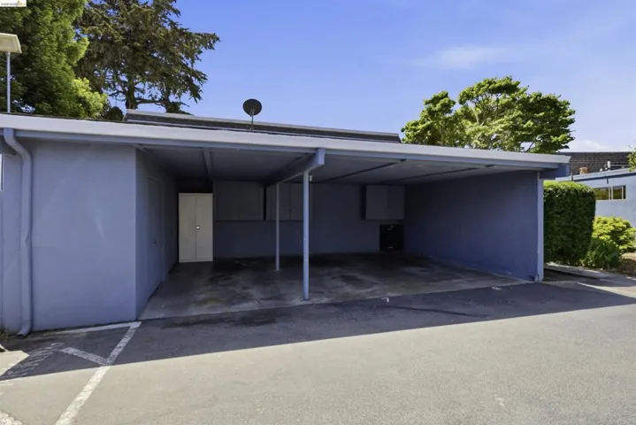 Covered carport providing sheltered parking, with an attached exterior storage unit featuring a white double door
