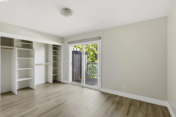 Room featuring wood-finish flooring, a sliding glass door leading to a balcony, and built-in closet shelving
