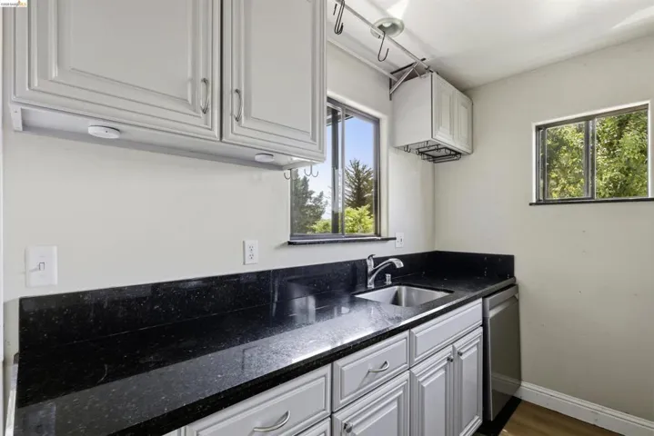 Kitchen area featuring light gray cabinetry, dark speckled countertops, and a stainless steel sink with a modern faucet