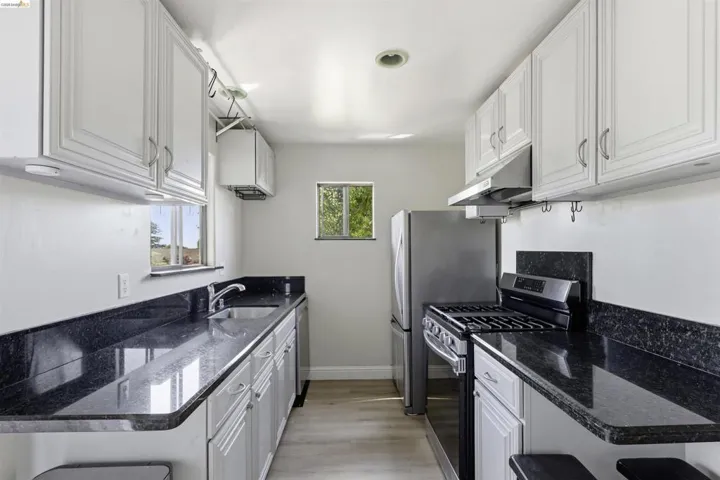 Galley kitchen featuring white cabinetry, dark stone countertops, stainless steel appliances, and light wood-finish flooring