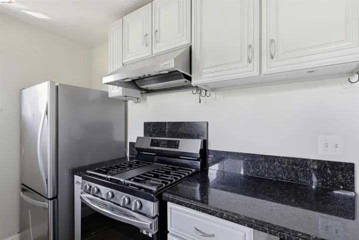 Kitchen featuring white cabinetry, stainless steel range with overhead hood, stainless steel refrigerator, and dark speckled countertops