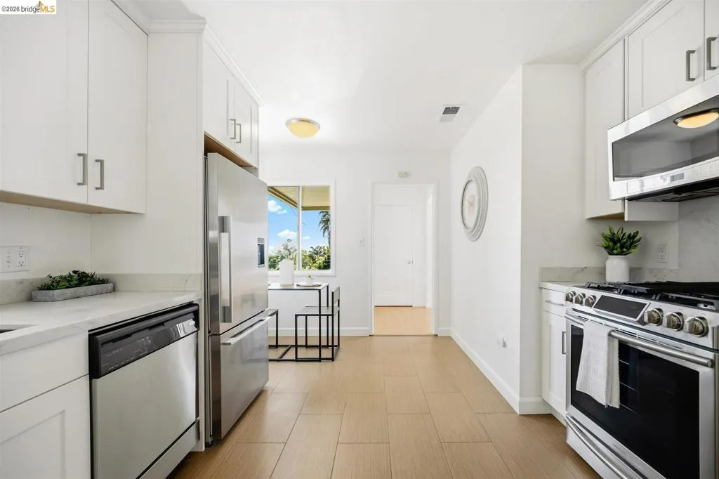 Bright kitchen featuring white cabinetry, stainless steel appliances, light-toned wood-finish flooring, and stone countertops