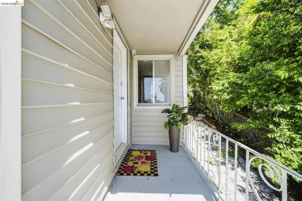 Covered exterior entry with siding, overhead lighting, and a white metal railing