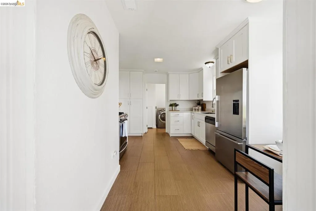Contemporary kitchen with wood-finish flooring, white cabinetry, stainless steel appliances, and a built-in stainless steel refrigerator