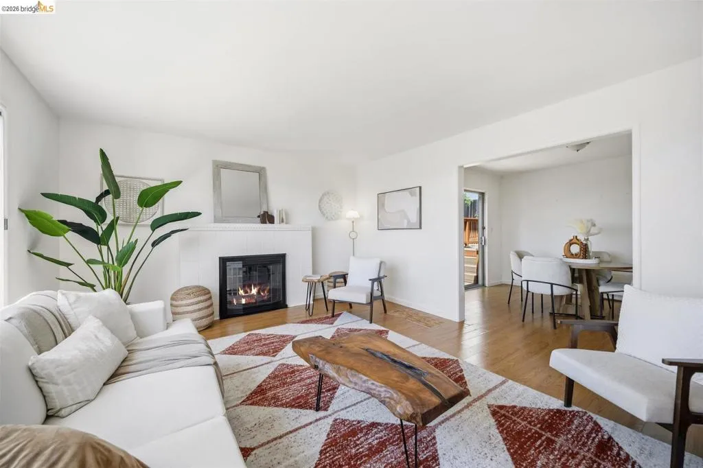 Living room with wood-finish flooring, a white tiled fireplace, and an open entryway to a dining area