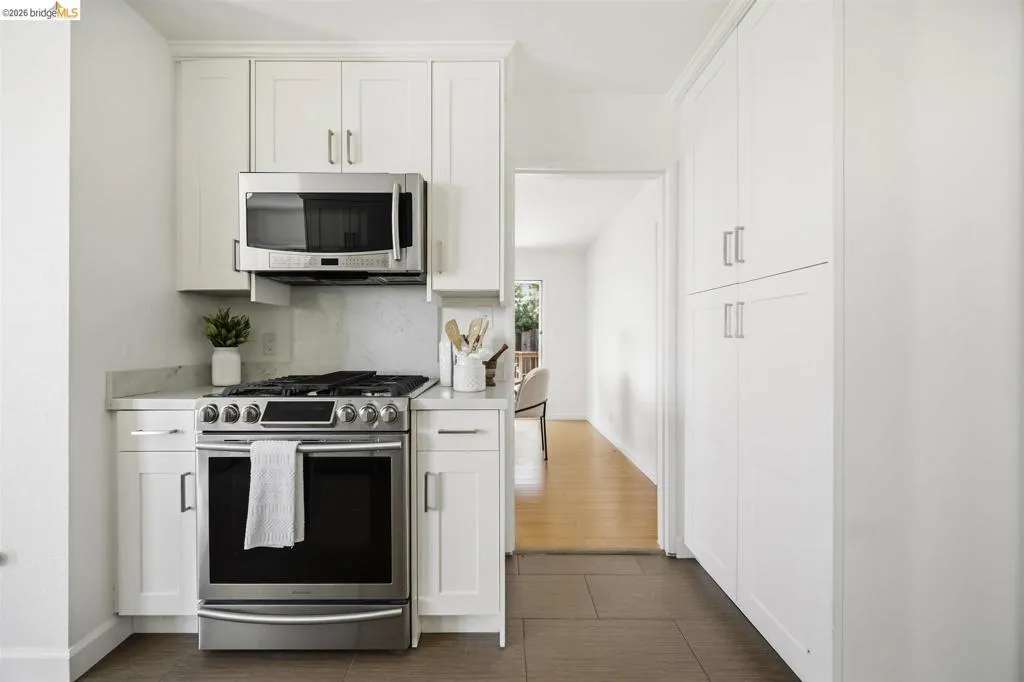 Kitchen featuring white shaker cabinetry, stainless steel range, stainless steel microwave with integrated ventilation, light-toned countertops, and a full-height tile backsplash