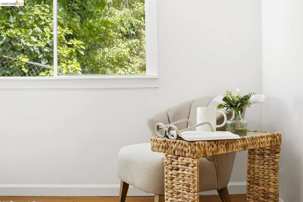 White walls with wood-finish flooring, featuring a large window with white trim and a neutral-toned accent chair