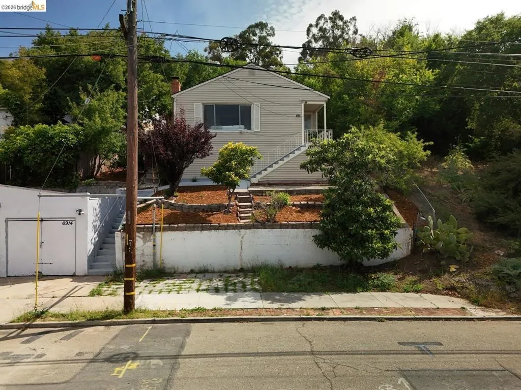Siding exterior with a covered entry, exterior staircase with metal handrails, and a multi-tiered front yard with landscaping