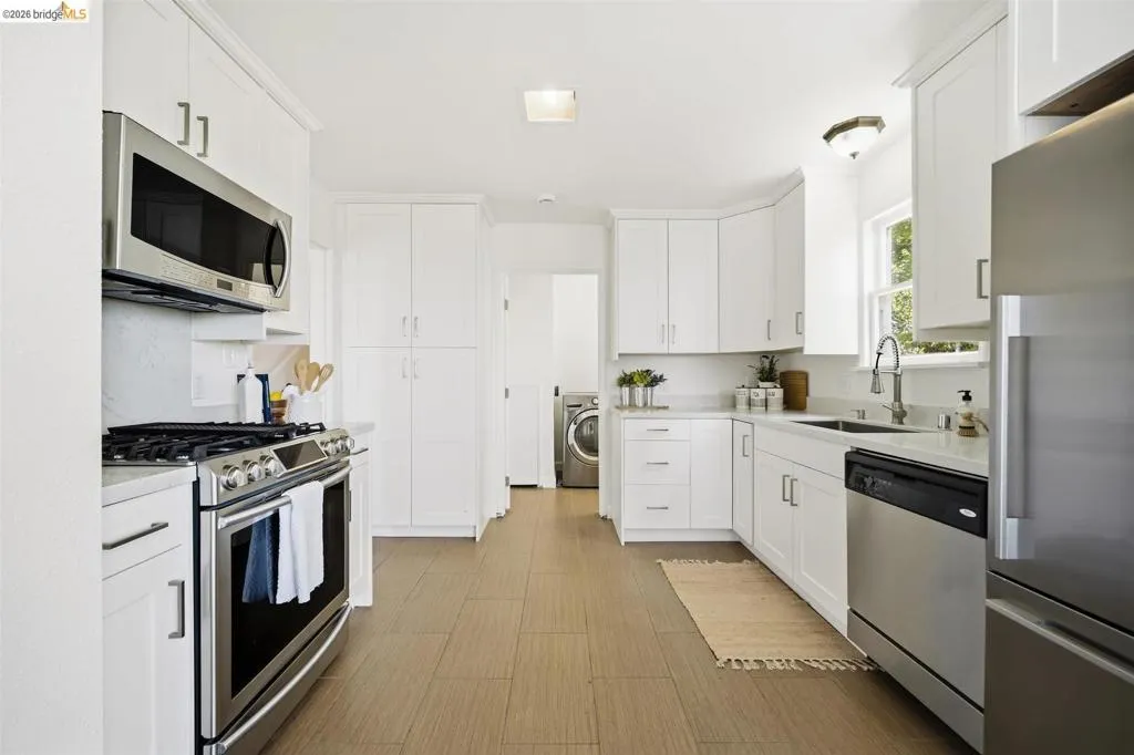 Modern kitchen featuring white cabinetry, stainless steel appliances, light-toned countertops, and wood-finish flooring