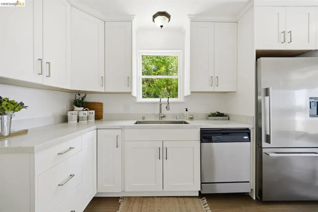 Bright kitchen featuring white shaker cabinetry, light countertops, stainless steel appliances, a window above the sink, and wood-finish flooring