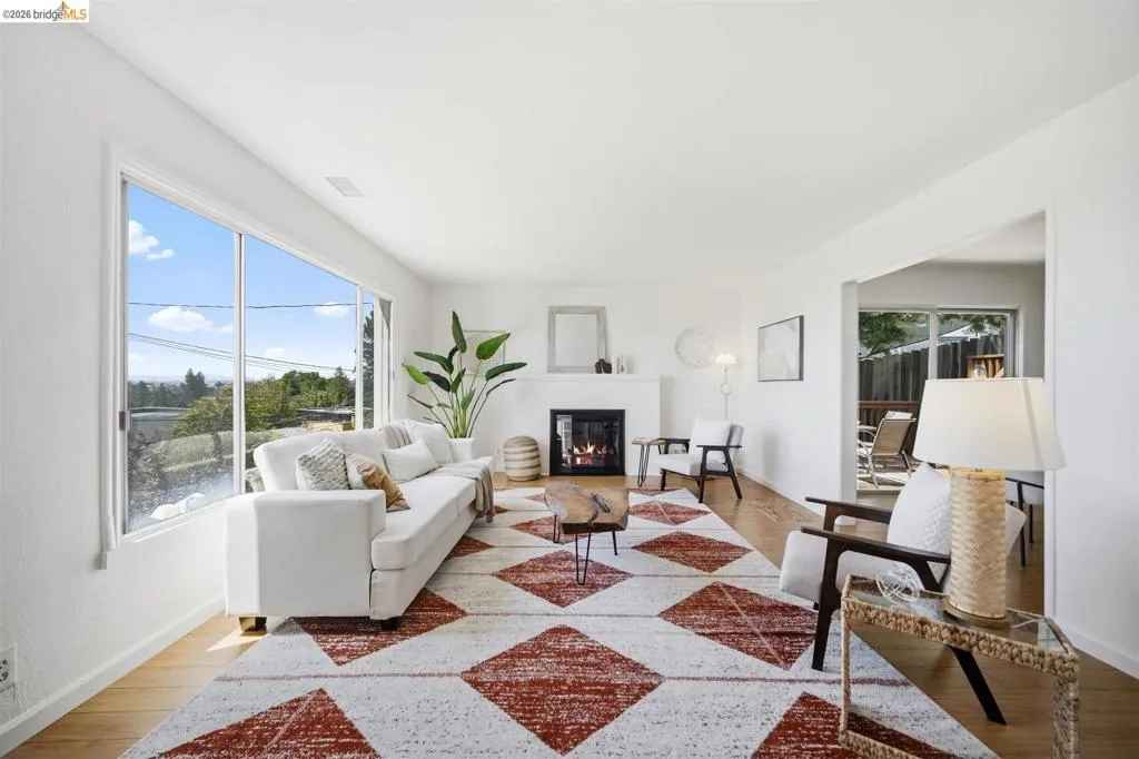 Living room featuring expansive window, wood-finish flooring, white walls, and a fireplace with a white mantel
