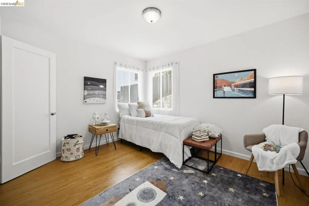 Bright bedroom featuring wood-finish flooring, white walls, and a corner window