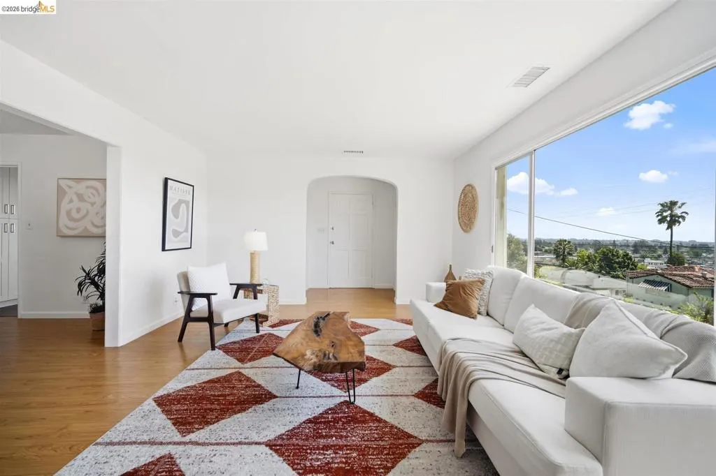 Expansive living area featuring wood-finish flooring, a broad picture window, an arched doorway, recessed lighting, and a cityscape backdrop