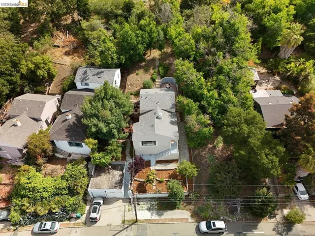 White exterior residence featuring a gray shingle roof, surrounded by mature trees and lush hillside landscaping