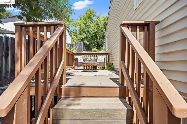 Multi-level outdoor deck featuring natural wood-tone railing and stairs, leading to an additional paved patio area, framed by horizontal siding