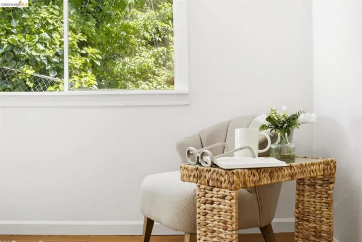 White walls with wood-finish flooring, featuring a large window with white trim and a neutral-toned accent chair