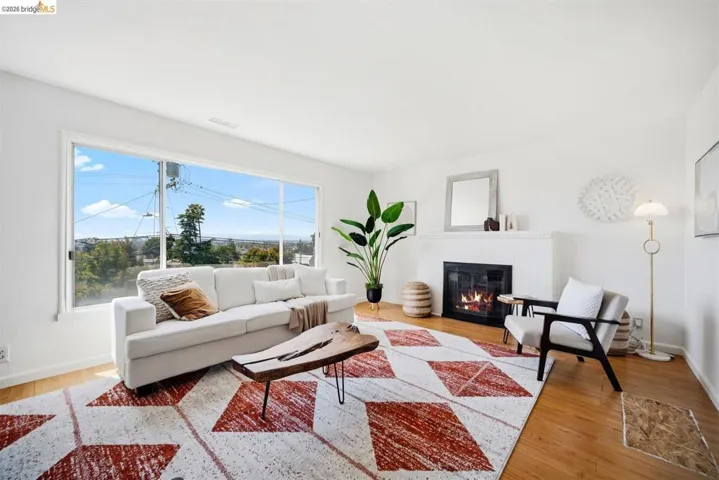Expansive windows illuminate this living space, featuring a fireplace with a white tile surround and wood-finish flooring