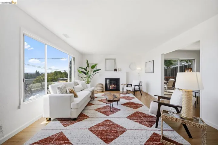 Living room featuring expansive window, wood-finish flooring, white walls, and a fireplace with a white mantel