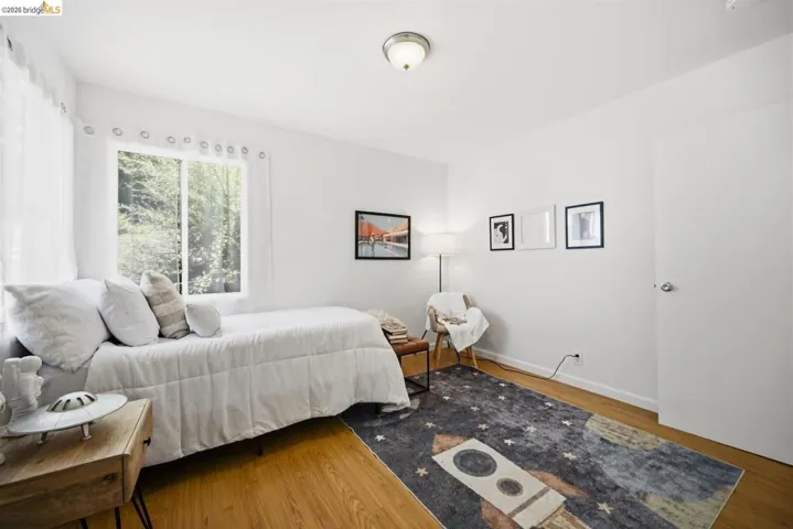 Room featuring light wood-finish flooring, white walls, and a large window with white sheer curtains