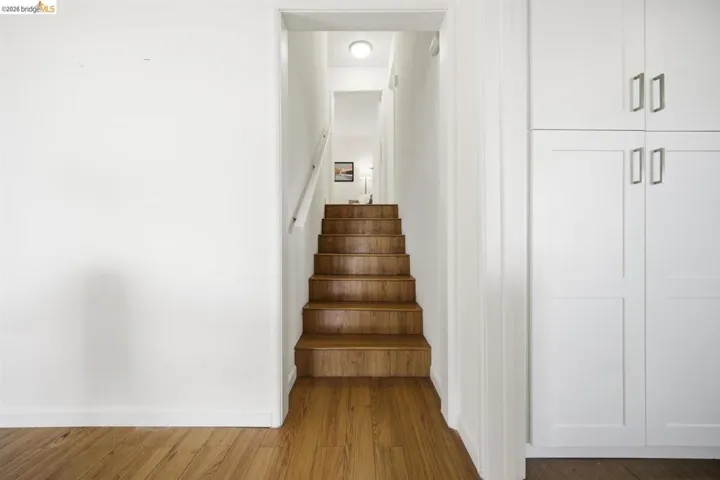 Wood-finish flooring extending to natural wood stairs with a white handrail