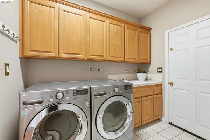 Utility space featuring light wood-finish cabinetry, a single basin sink with chrome faucet, tiled flooring, and a paneled white door