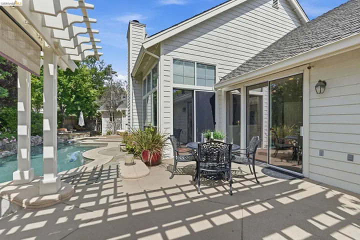 Expansive outdoor patio with a pergola, featuring a built-in pool, concrete decking, and multiple sliding glass doors for indoor-outdoor living