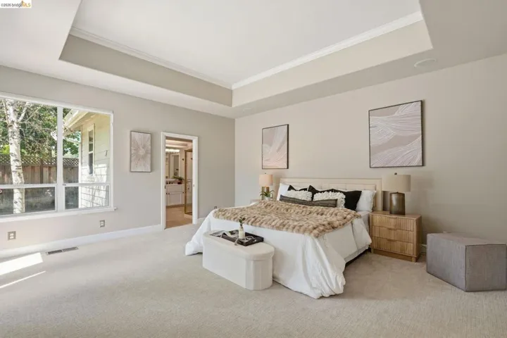 Spacious bedroom featuring light-toned carpeting, a tray ceiling with crown molding, and large multi-pane windows
