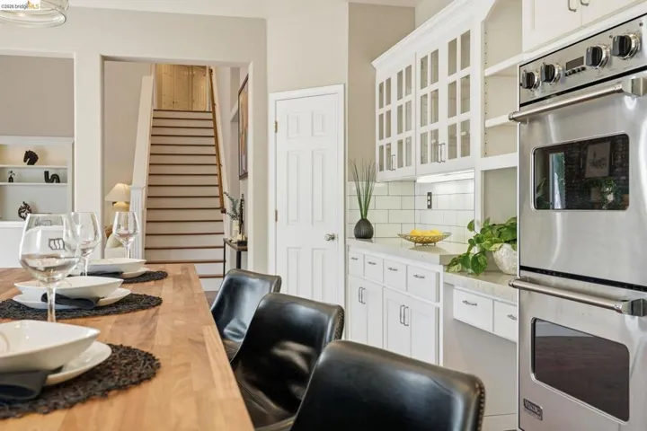 Gourmet kitchen featuring double wall ovens, white cabinetry with glass-front uppers, and solid surface countertops