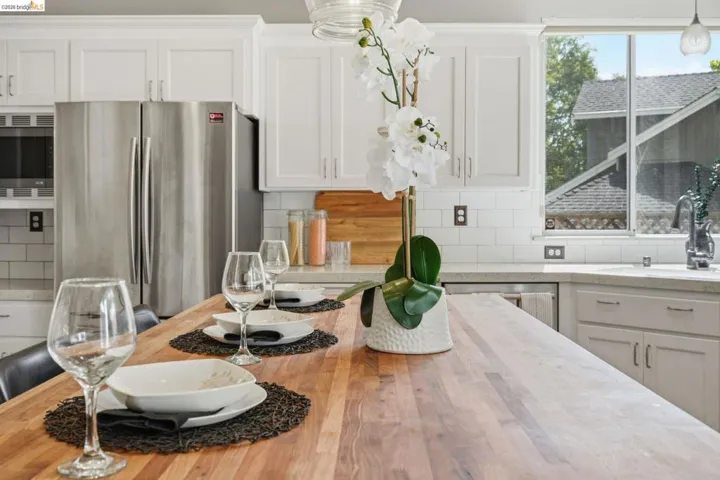 Kitchen featuring a spacious wood-finish island, white shaker cabinetry, stainless steel refrigerator, white subway tile backsplash, and light-colored countertops
