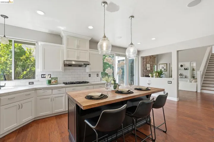 Contemporary kitchen featuring a large center island with a wood-finish countertop, white shaker cabinetry, subway tile backsplash, and recessed lighting