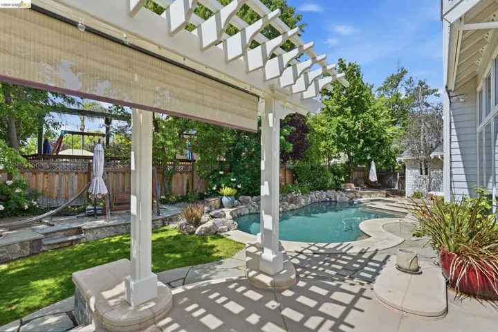 Patio area featuring a white pergola with a retractable shade