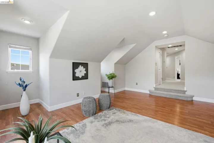Spacious attic bonus room with warm wood-finish flooring, recessed lighting, and a white framed window
