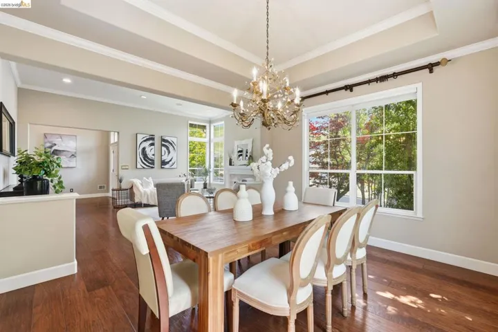 Open-concept dining area featuring wood-finish flooring, a coffered ceiling with crown molding, and a chandelier