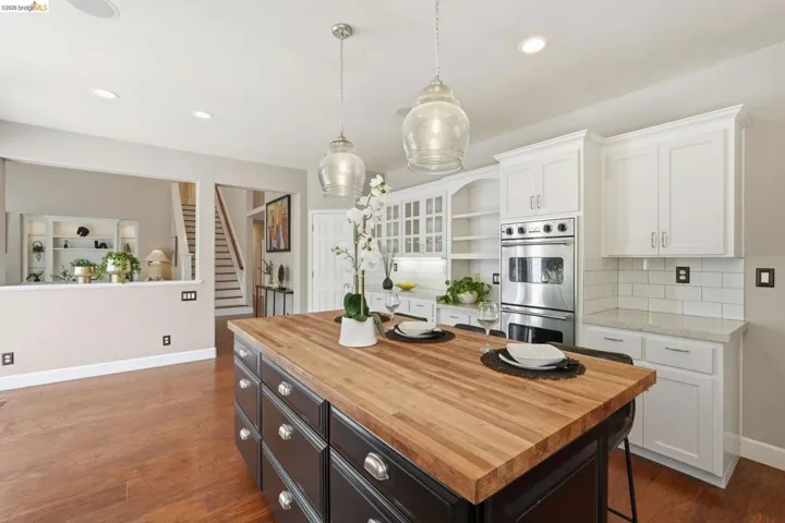 Kitchen featuring a spacious island with a butcher block countertop, white shaker cabinetry, stainless steel double ovens, and subway tile backsplash
