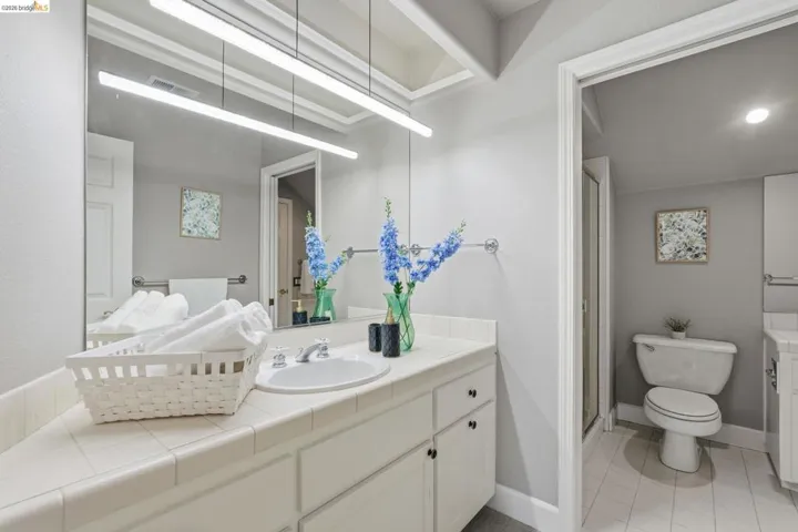 Bathroom vanity with white tile countertop, integrated sink, and white cabinetry