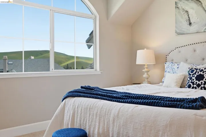 Room featuring a large arched window with grid patterns, a neutral color palette, sloped ceiling, and an upholstered headboard with nailhead trim