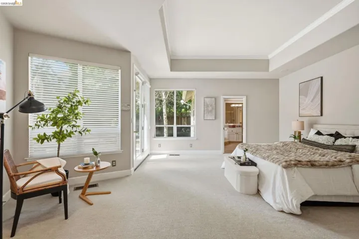Spacious room featuring light-toned carpeting, ample natural light from multiple windows with horizontal blinds, and a tray ceiling with crown molding