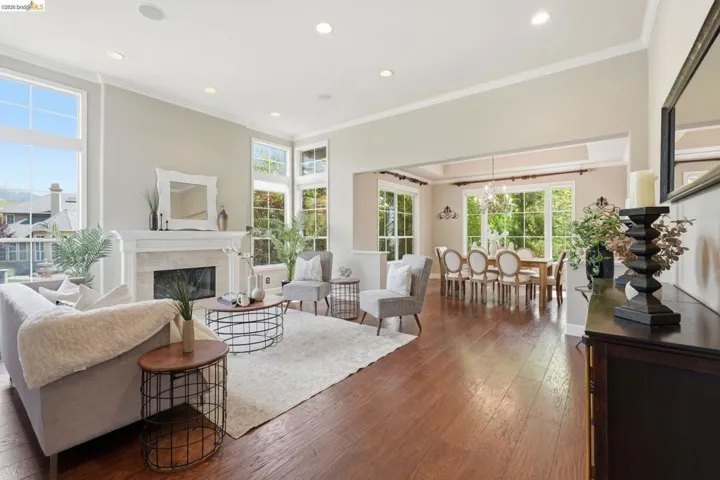 Expansive living space featuring rich wood-finish flooring, a white stone-surround fireplace with a classic mantel, and tall windows
