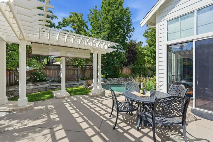 Expansive patio featuring a white pergola with a retractable shade, concrete flooring, and a nearby pool