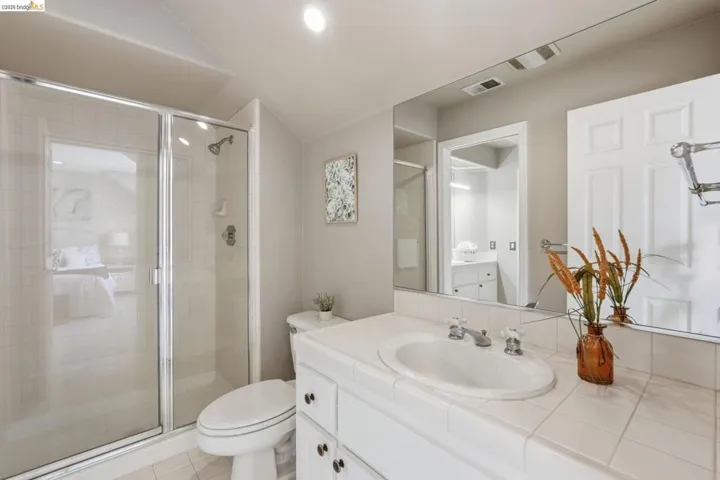 Bathroom featuring a glass-enclosed shower, white tile flooring, white vanity with integrated sink, and an expansive wall-mounted mirror