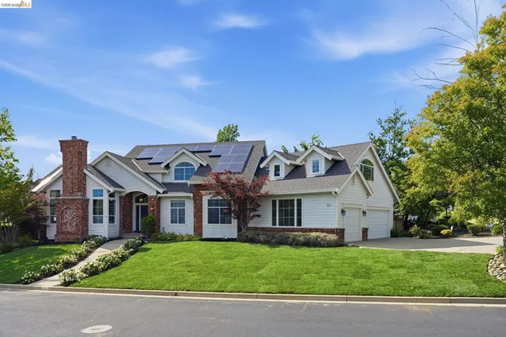 Traditional-style residence featuring a prominent brick chimney, multiple solar panels on the roof, and a two-car garage