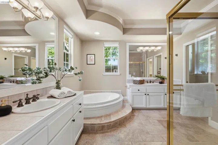 Bathroom featuring a built-in soaking tub, dual vanity with undermount sinks, separate glass-enclosed shower, and decorative tray ceiling
