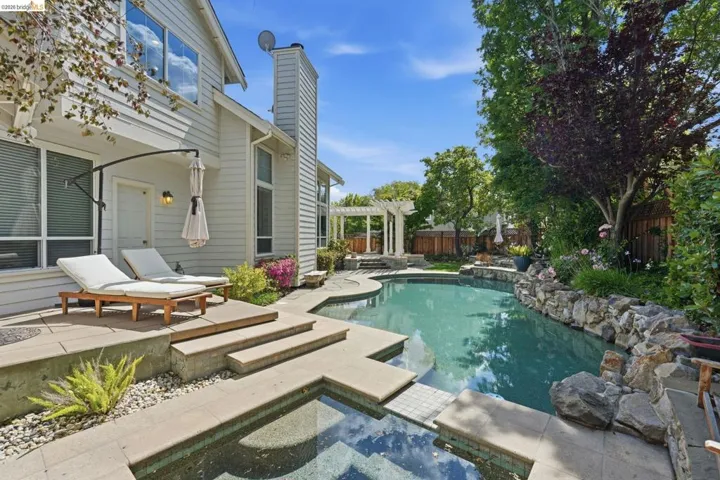 Backyard oasis featuring a curvilinear pool, integrated spa, and an expansive paved patio